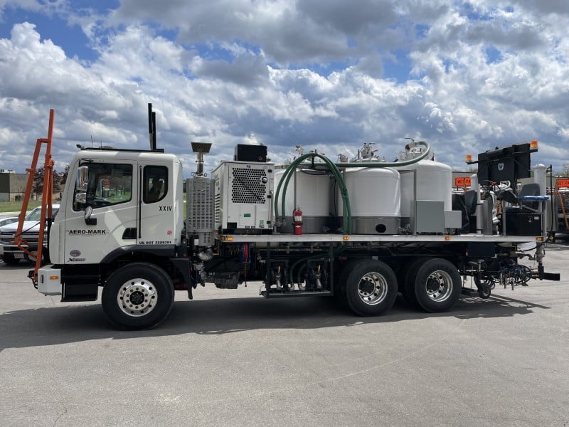A large industrial truck branded with “Aero Mark” on the driver side door with cylindrical tanks and equipment on its flatbed is parked on a paved surface under a cloudy sky