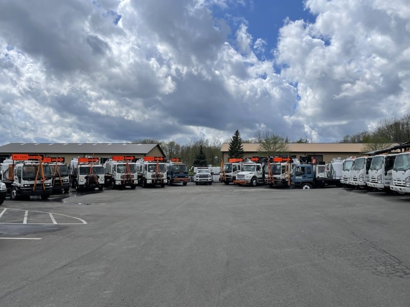 A row of Aero-Mark maintenance trucks with bright orange signs reading "WET PAINT KEEP RIGHT," parked in front of an industrial building on a cloudy day