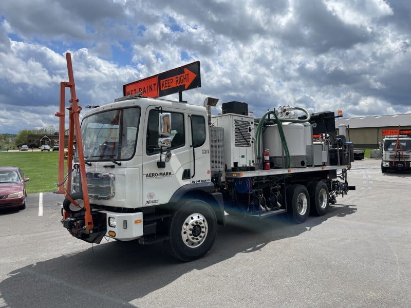A specialized work truck with mounted equipment and a "WET PAINT KEEP RIGHT" sign.